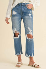 Distressed raw hem cropped jeans with ripped knees, styled casually with a loose sweater and sandals.