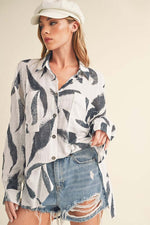 Model in a high-low printed button-up shirt paired with distressed denim shorts for a trendy look.