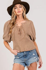 Stylish woman in a brown lace-up waffle knit crop top and denim shorts, accessorized with a wide-brim hat.