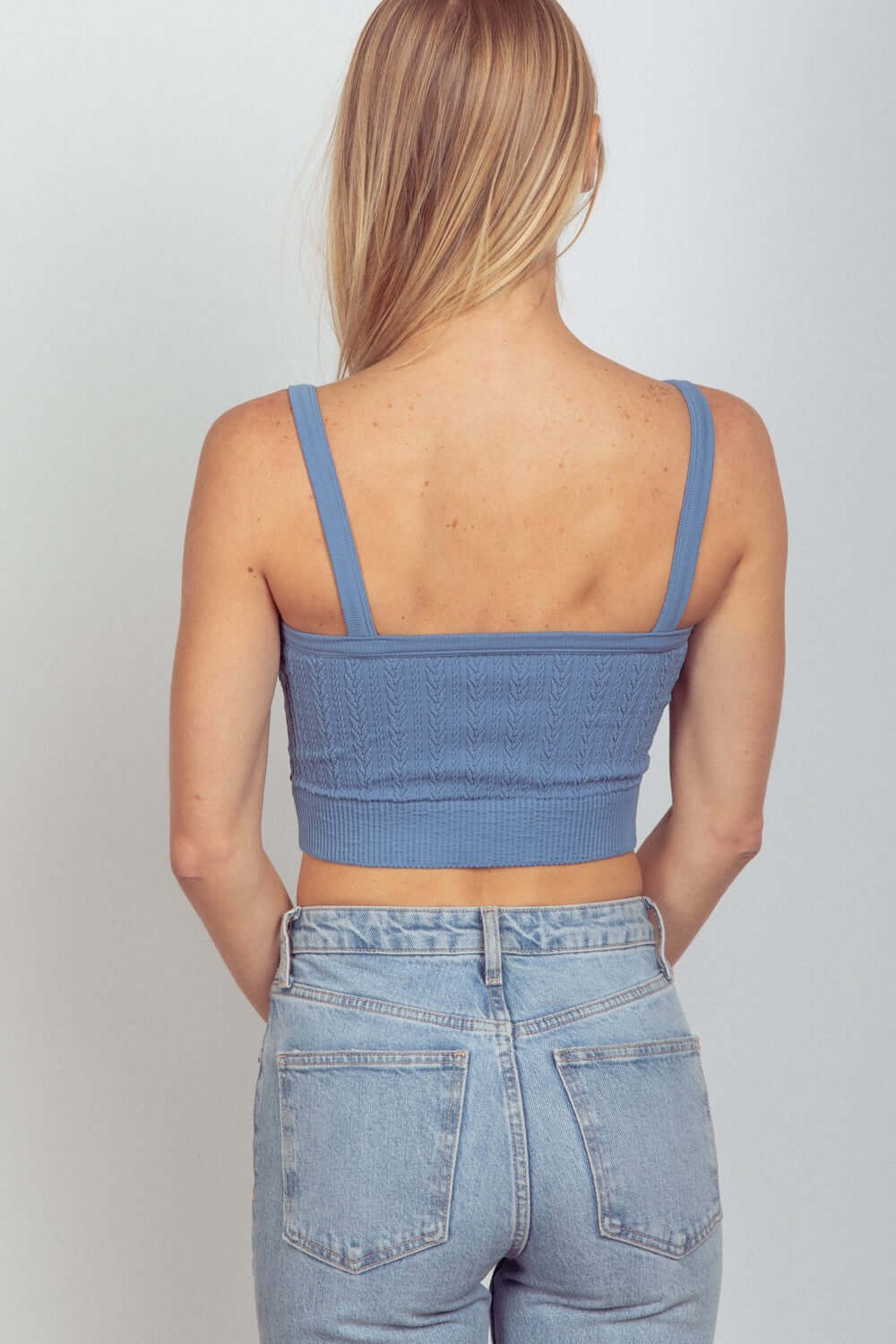 Woman wearing blue cable knit seamless cropped cami with high-waisted jeans, showing back view.