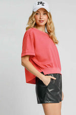 Plus size lightweight cropped sweatshirt in coral, styled with black shorts and a NY cap, exuding trendy vibes.