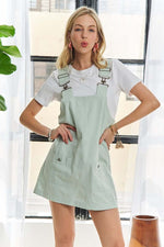 Woman in light green adjustable overall dress paired with a white tee, stylish and chic for casual wear.