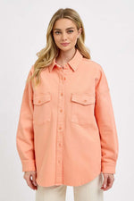 Stylish woman wearing a peach RISEN button-down long sleeve denim shacket with chest pockets.