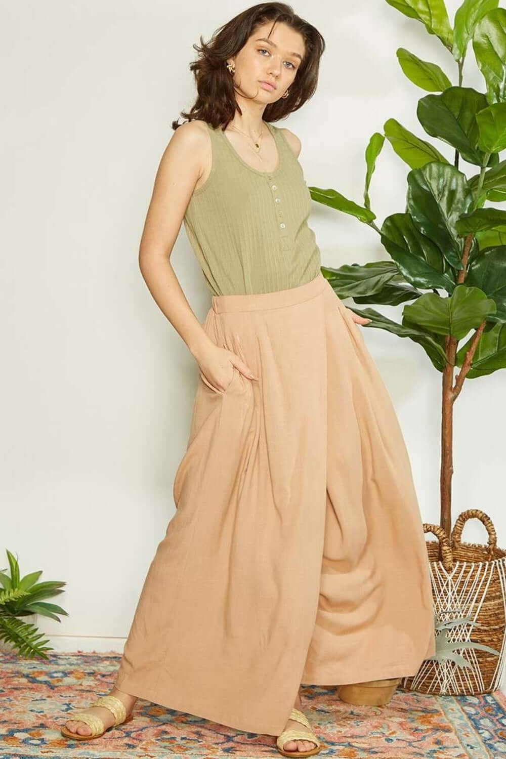 Woman wearing wrap pleating detail wide leg pants in a chic, modern outfit with a green top, standing beside indoor plants.