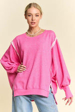 Woman in pink lantern sleeve knit top with side slits, showcasing trendy high-low design and relaxed fit.