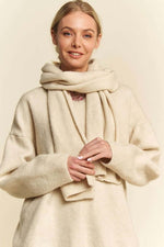 Woman in a cozy beige V-neck sweater with dropped shoulders and matching scarf, exuding warmth and style.