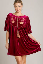 Elegant woman wearing a red velvet mini dress with embroidered flowers and tassels, perfect for special events.