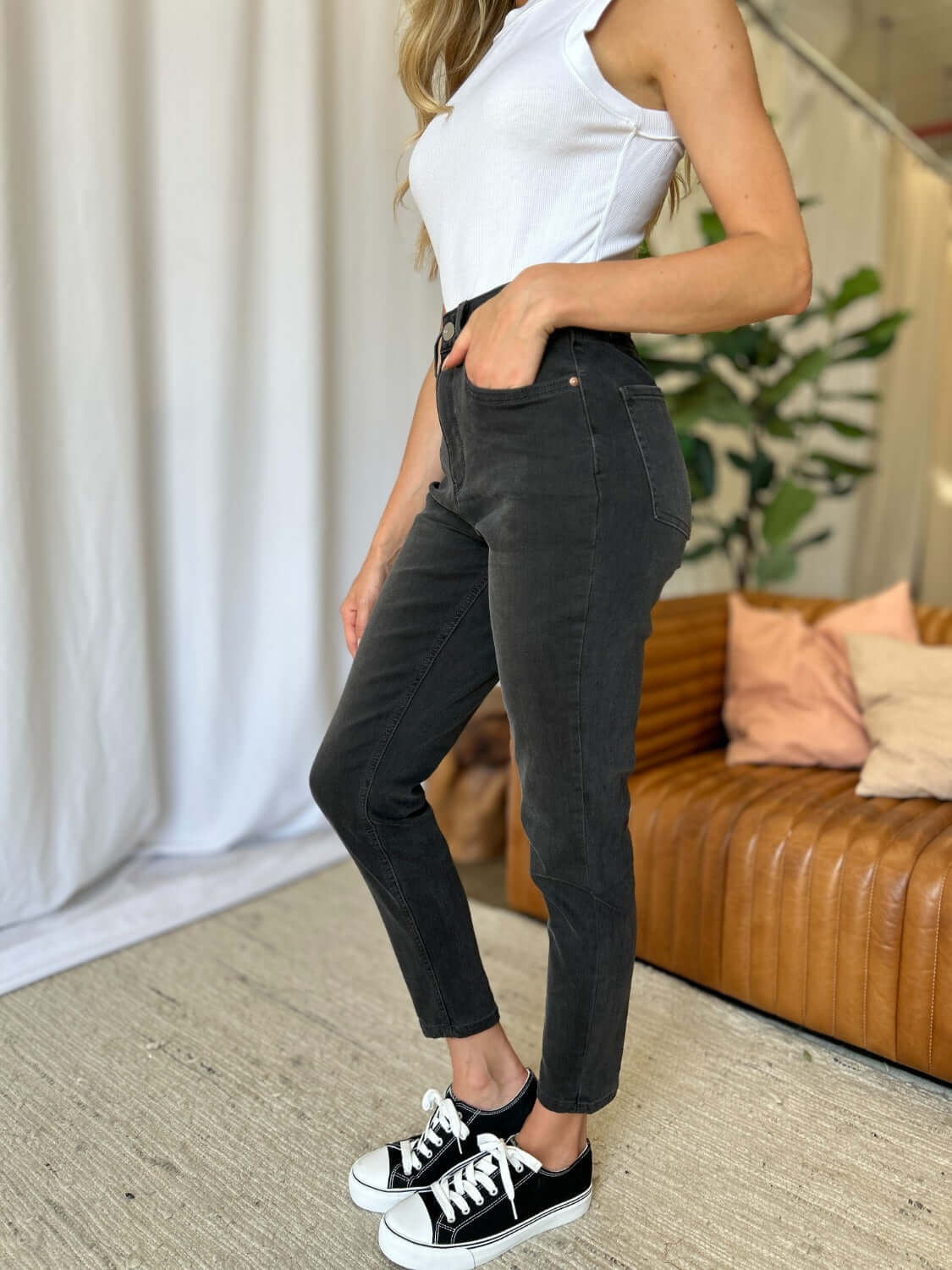 Model wearing high rise tummy control skinny jeans in black, paired with a white tank top and black sneakers, demonstrating a sleek and modern look