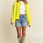 Woman models a yellow snap-down long sleeve shacket with high-low hem, styled with denim shorts, white top, and knee-high boots.