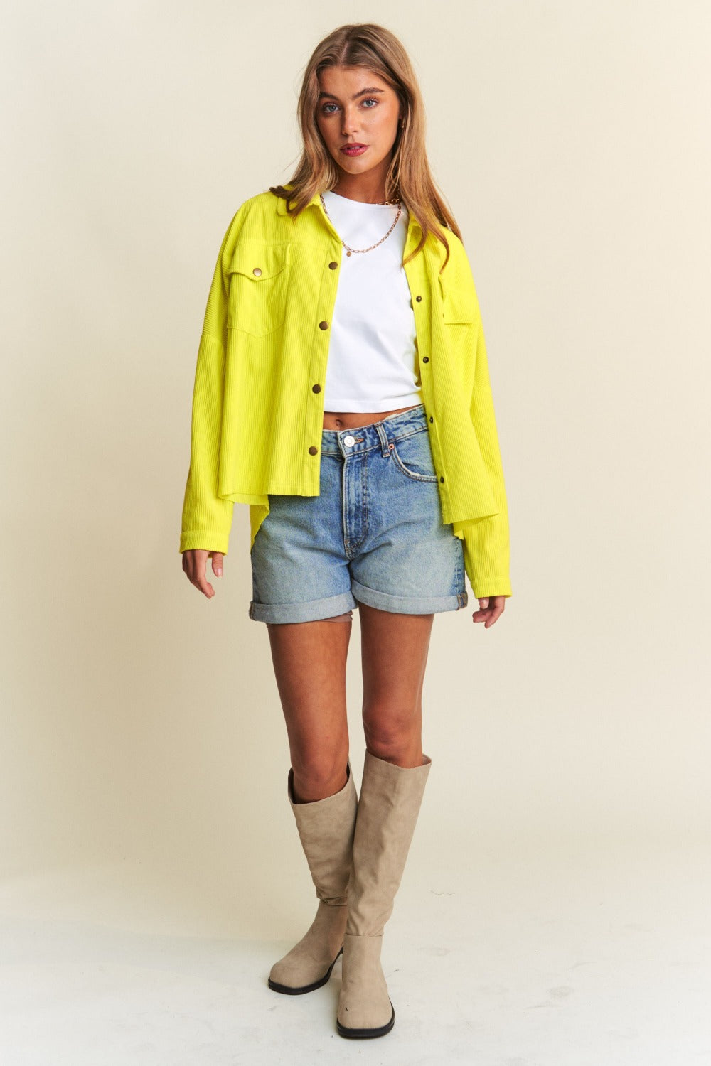 Woman models a yellow snap-down long sleeve shacket with high-low hem, styled with denim shorts, white top, and knee-high boots.