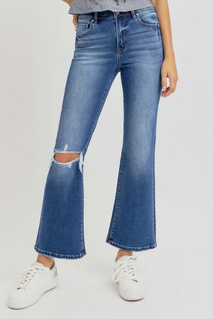 Risen distressed high rise crop flare jeans with trendy ripped knee detail, styled with white sneakers for a chic casual look.