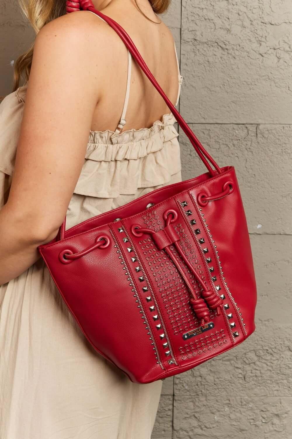 Woman holding Nicole Lee USA Amy Studded Bucket Bag in red vegan leather with stud and zipper detailing