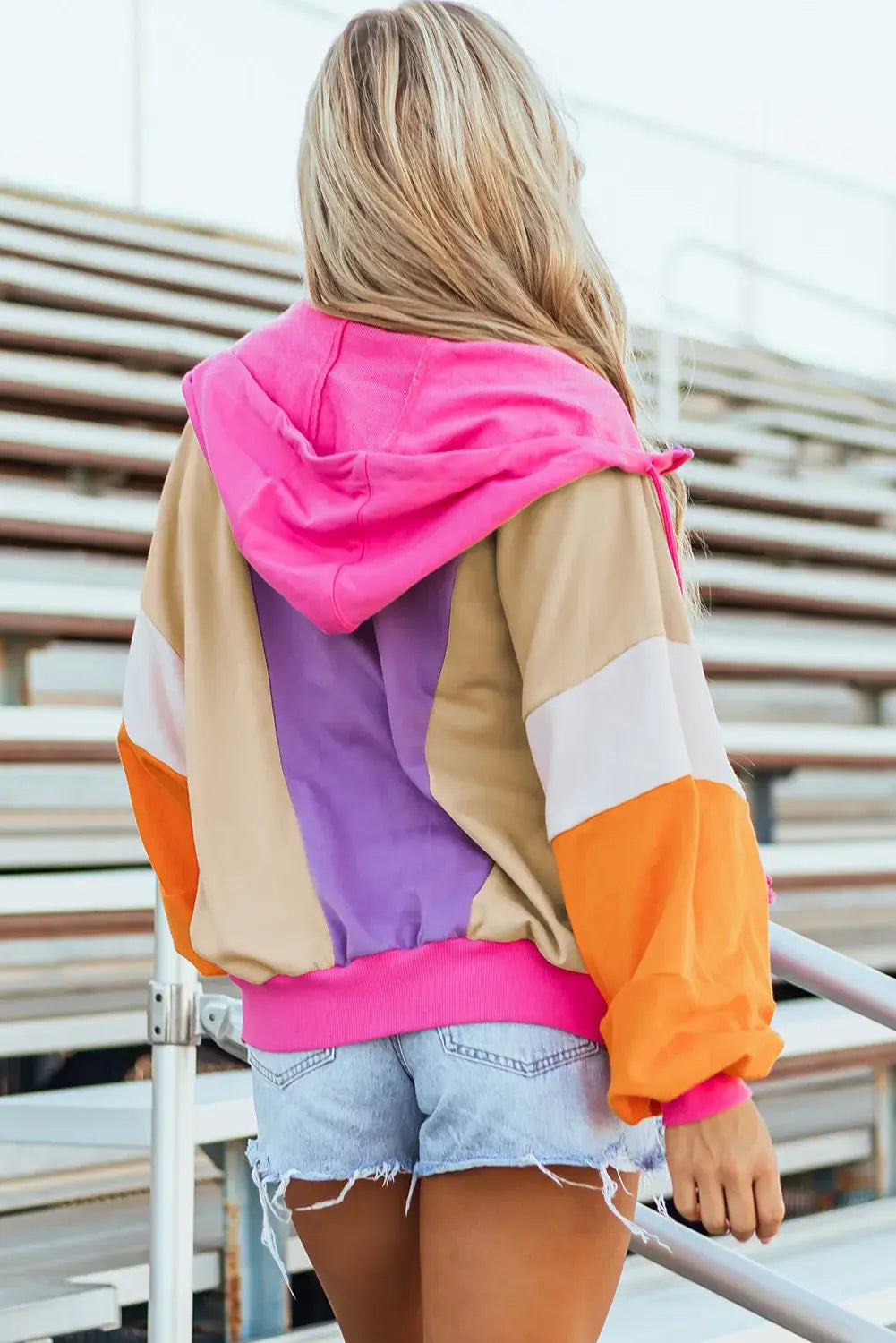 Woman wearing a Drawstring Color Block Zip Up Long Sleeve Hoodie with denim shorts, featuring vibrant pink, purple, beige, and orange sections.