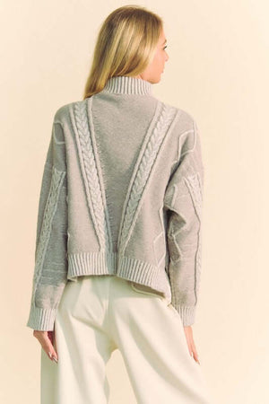 Back view of a cozy Davi & Dani cable-knit turtleneck sweater, featuring a dropped shoulder design and stylish ribbed details.