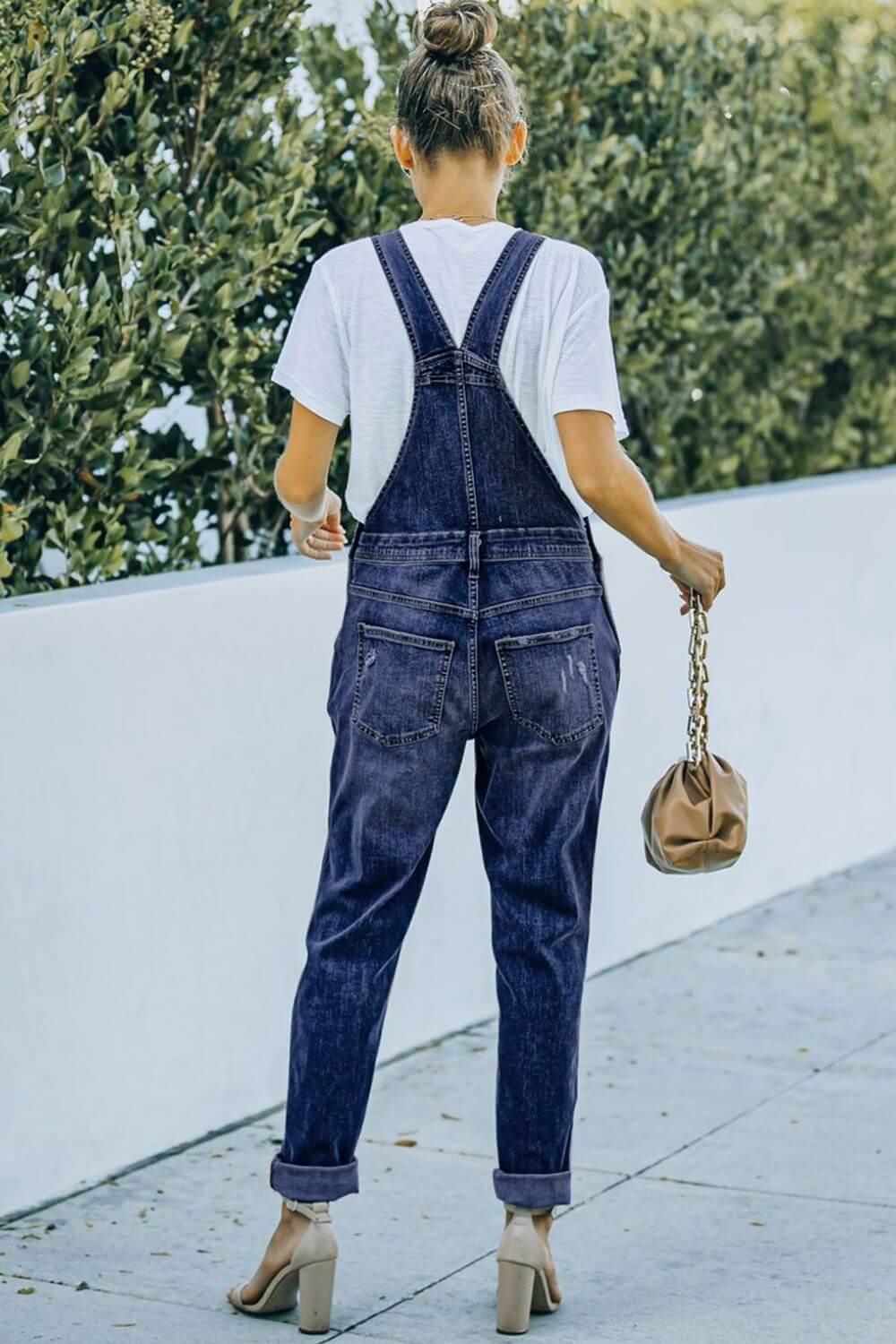 Woman wearing pocketed distressed denim overalls with acid wash pattern outdoors. Casual girl-next-door style with slight stretch.