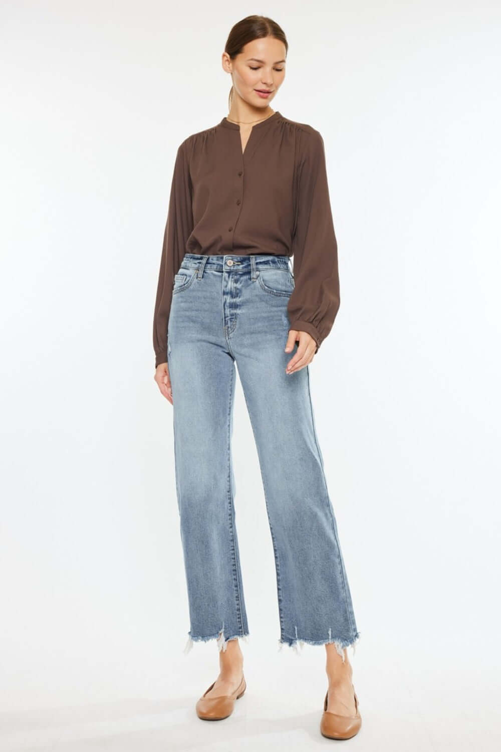 Woman wearing Kancan high rise slim wide leg jeans in light wash, styled with a brown blouse, highlighting unique hem details.