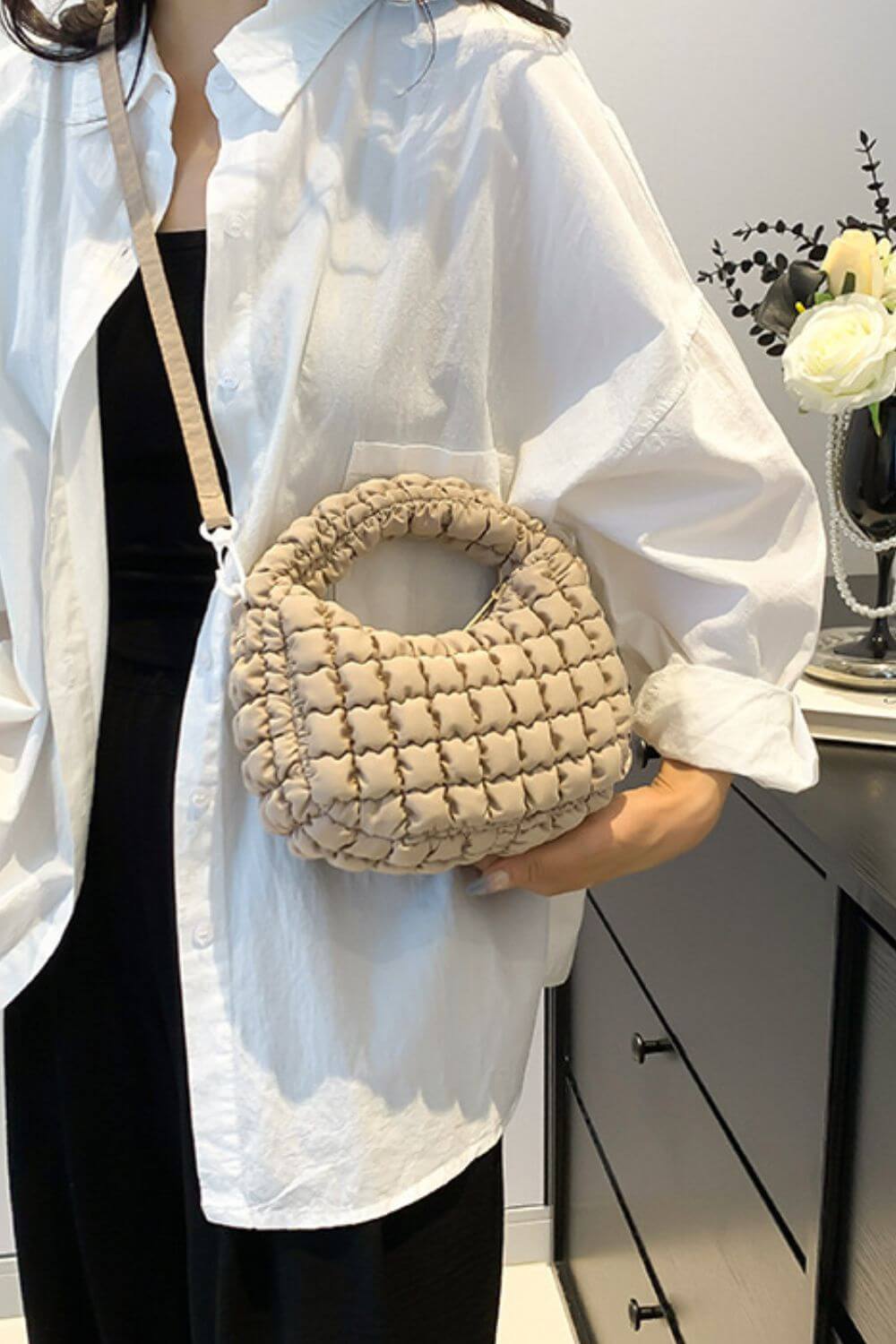 Woman holding Bella Road quilted puffy crossbody bag with removable strap, featuring unique design, displayed in modern room.