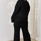 Curve model wearing black ribbed high-low top and wide leg pants set, showing back view.