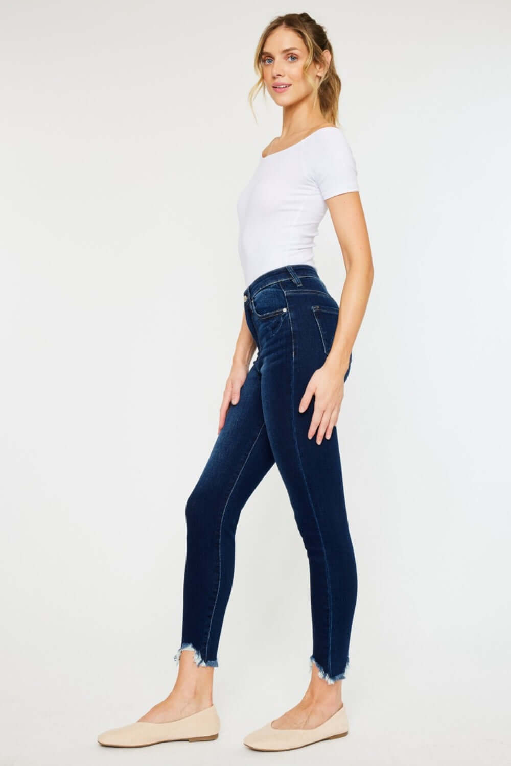 Woman wearing High Rise Frayed Ankle Skinny Jeans, side profile view showcasing the trendy ankle-length frayed hem and flattering high-waist fit.