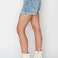 Stylish woman modeling distressed mid-rise waist denim shorts by Risen Jeans with white ankle boots