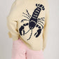 Woman wearing Bella Road Lobster Button Up Long Sleeve Cardigan with playful lobster design on back. Perfect for a touch of fun.