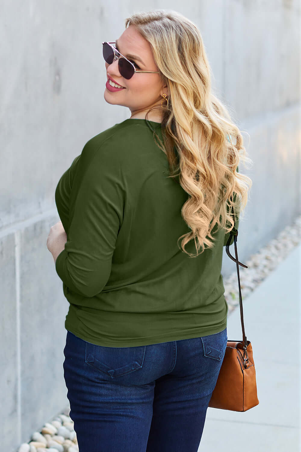 Plus-size model wearing round neck batwing sleeve top in green, paired with blue jeans and brown handbag