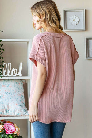 Woman wearing Exposed Seam Short Sleeve Ribbed Top in pink with jeans, showcasing back view in a modern home setting