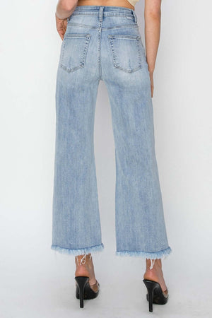 Woman wearing Risen high rise crop jeans with wide fray hem, showcasing trendy and edgy fashion in a relaxed fit.