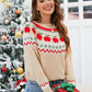 Woman wearing angel wings sweater with apple graphic, smiling by Christmas tree, holding gift box. Perfect holiday fashion.