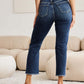 Woman wearing RFM Jeans Crop Dylan Full Size Tummy Control Distressed High Waist Raw Hem Jeans, stylish backside view in modern living room