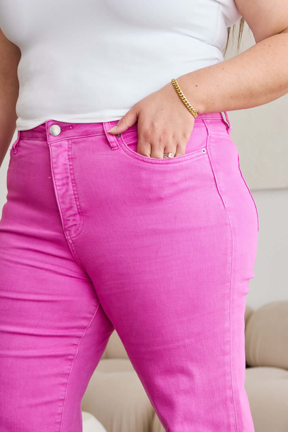 Woman wearing pink RFM Jeans with high waist and tummy control features, showing stylish raw hem and gold bracelet.