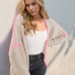 Woman wearing Double Take Contrast Cardigan with open front and dropped shoulders in beige with pink accents, posing stylishly.