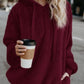 Stylish woman wearing a burgundy teddy hoodie with drawstrings, holding a coffee cup on a city street.