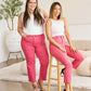 Two women wearing pink high-waisted jeans and white tops, showcasing RFM Jeans with a stylish raw hem design in a modern and comfortable setting.