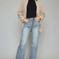 Trendy woman wearing high waist raw hem cropped wide leg jeans with black top and beige jacket, showcasing chic and modern style.