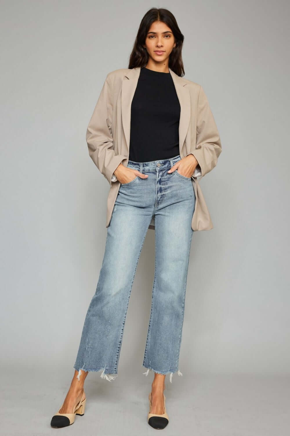 Trendy woman wearing high waist raw hem cropped wide leg jeans with black top and beige jacket, showcasing chic and modern style.