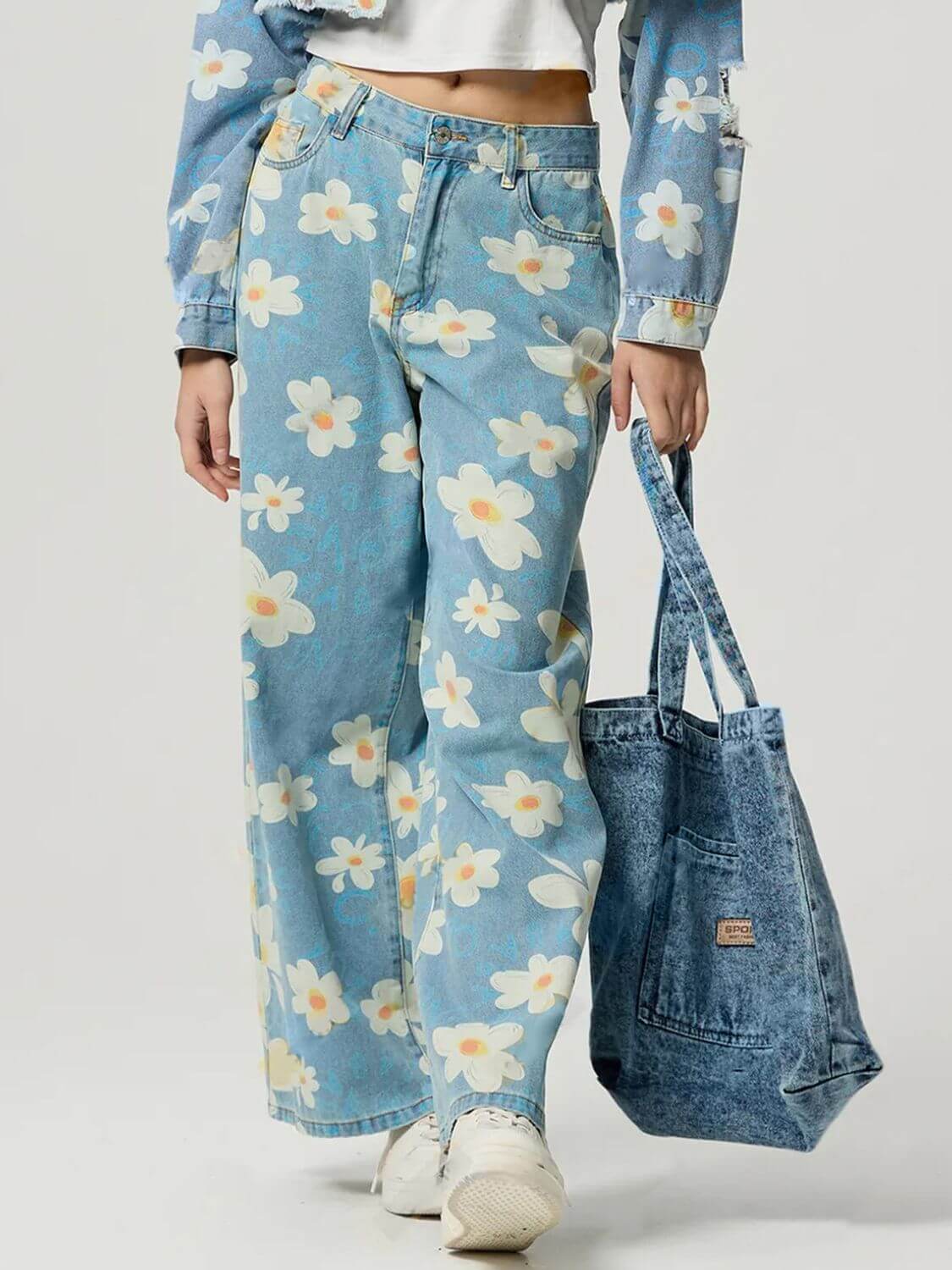 Model showcasing Bella Road denim pocketed floral wide leg jeans with a blue floral pattern and matching tote bag.