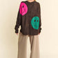 Back view of Davi & Dani oversized sweater with pink and green smiley faces, paired with relaxed beige pants.