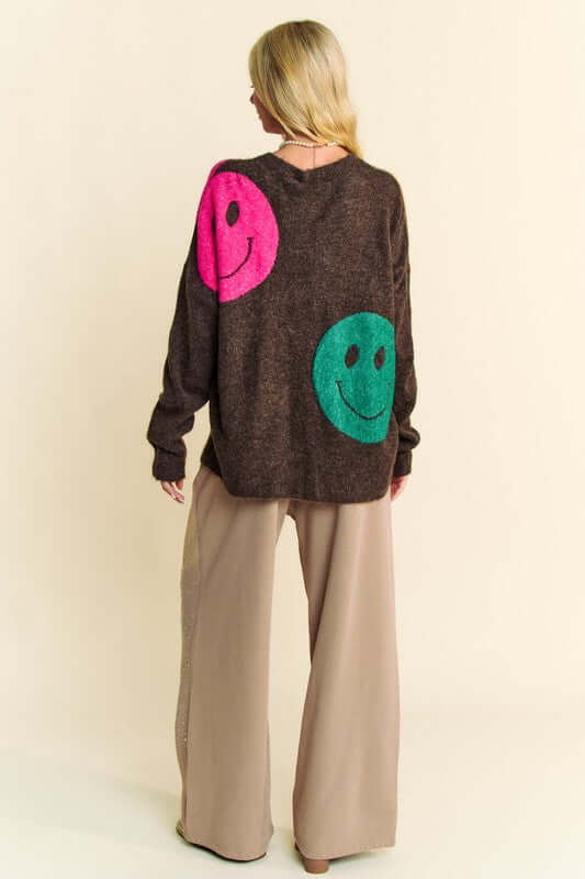 Back view of Davi & Dani oversized sweater with pink and green smiley faces, paired with relaxed beige pants.