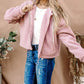 Woman wearing And The Why Sherpa Drawstring Cropped Hooded Jacket in pink, standing outdoors, pairing it with blue jeans.