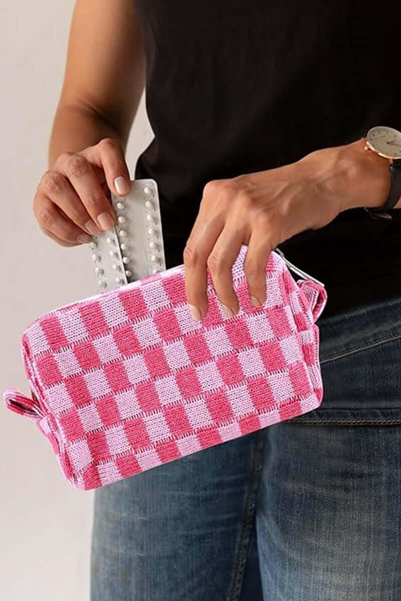 Woman holding a pink checkered knitted cosmetic pouch with zipper, showcasing its stylish and functional design.