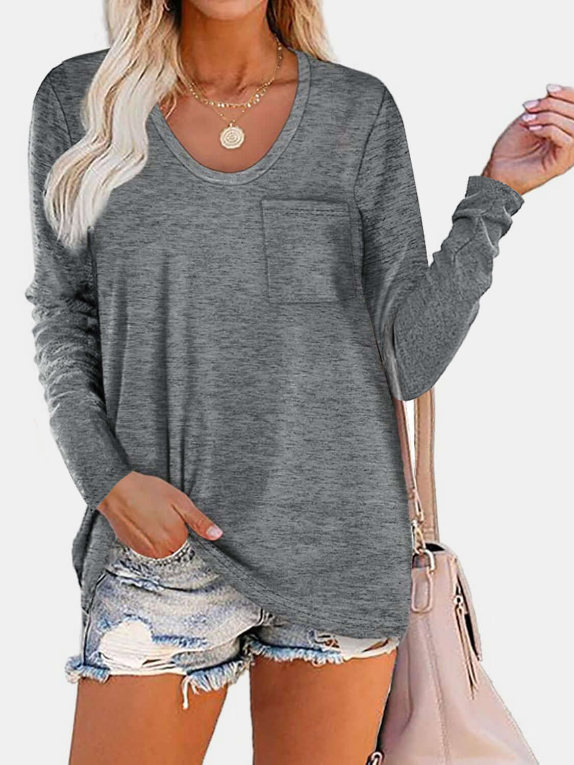 Woman wearing Bella Road gray round neck long sleeve T-shirt with pocket, paired with ripped denim shorts and carrying a beige handbag.