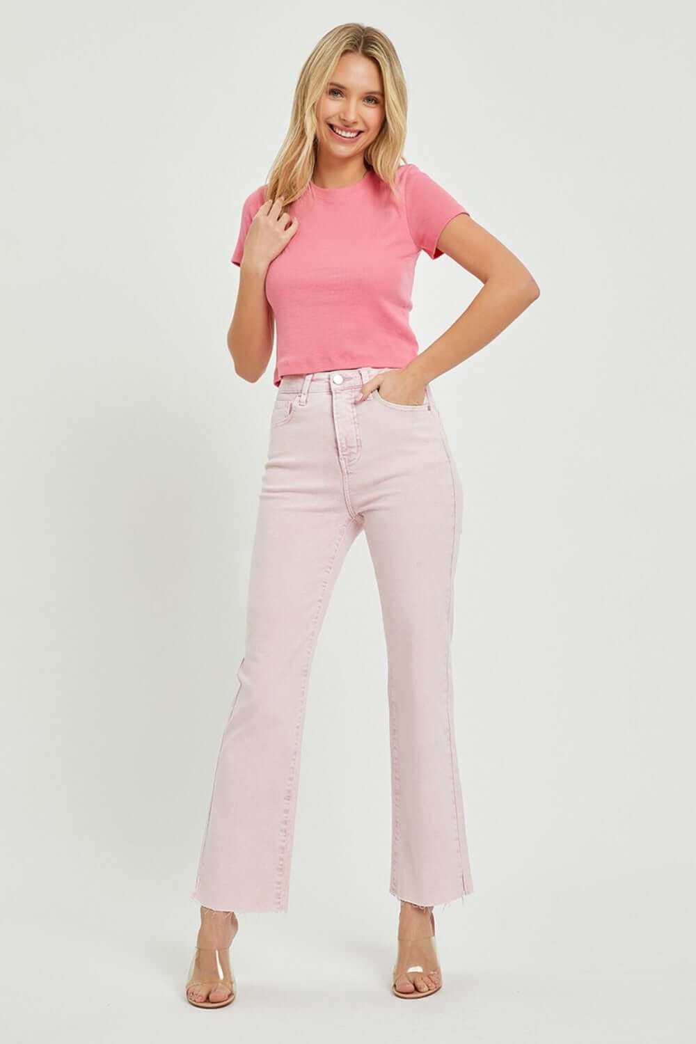 Woman wearing RISEN Full Size High Rise Tummy Control Straight Jeans in light pink with raw hem, paired with a pink t-shirt and high heels.