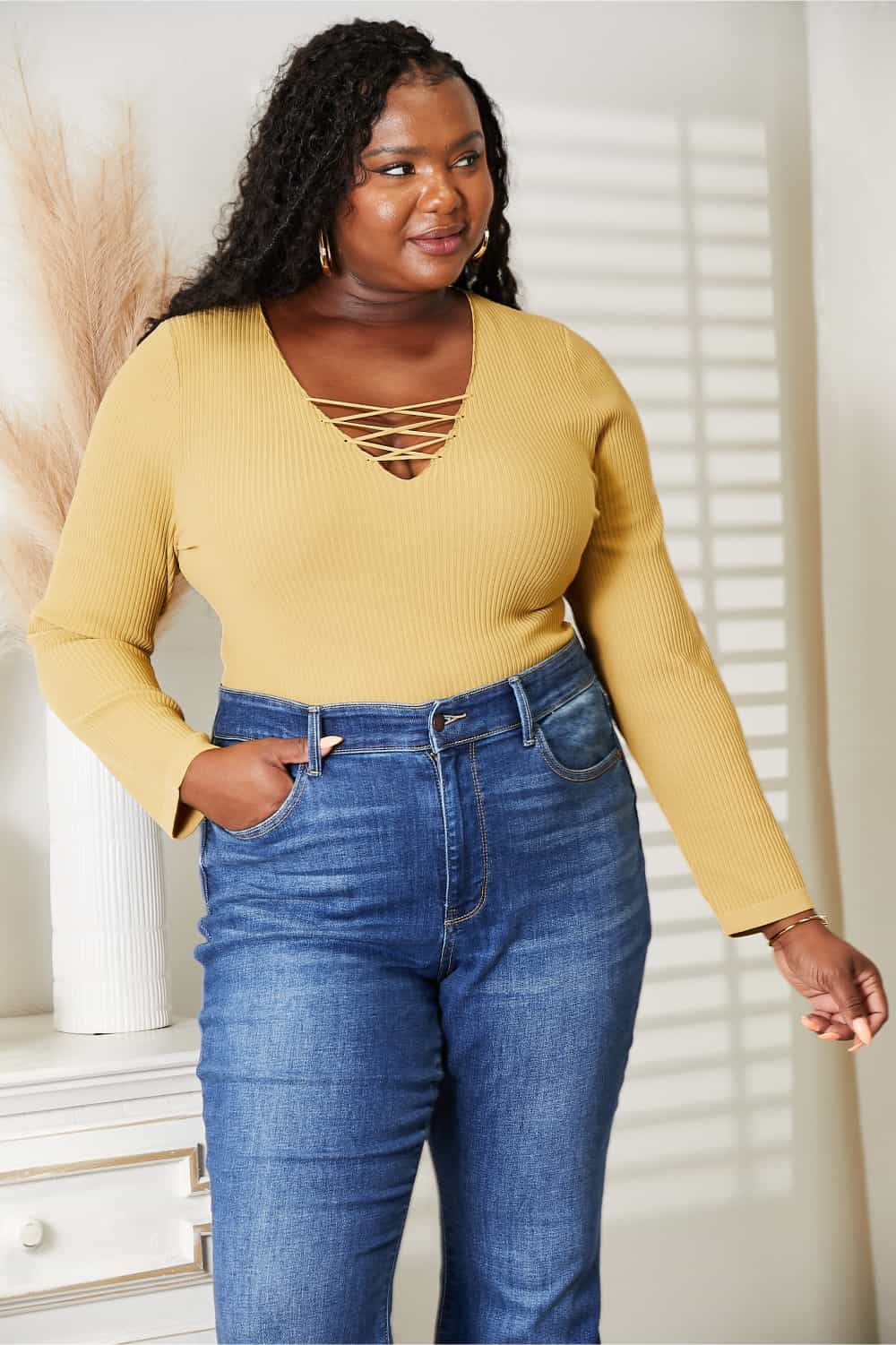 Woman wearing All About Details ribbed bodysuit with lace-up caged neck detail, paired with high-waisted jeans, posing in a room.