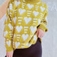 Woman wearing Bella Road Heart Contrast Long Sleeve Dropped Shoulder Sweater with playful white heart design against a vibrant yellow background.