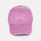 Pink bow embroidered washed cotton cap with delicate white bow design, stylish and comfortable headwear for a playful and elegant look.