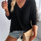 Woman wearing Double Take Pocketed Textured V-Neck Long Sleeve T-Shirt with denim shorts and holding a beige clutch.