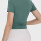 Back view of a woman wearing a green Millennia Ruched Round Neck Short Sleeve Active T-Shirt, paired with light pants.