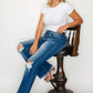 Woman in a white tee and raw hem distressed bootcut jeans sitting on a stool, showcasing a trendy and casual look.