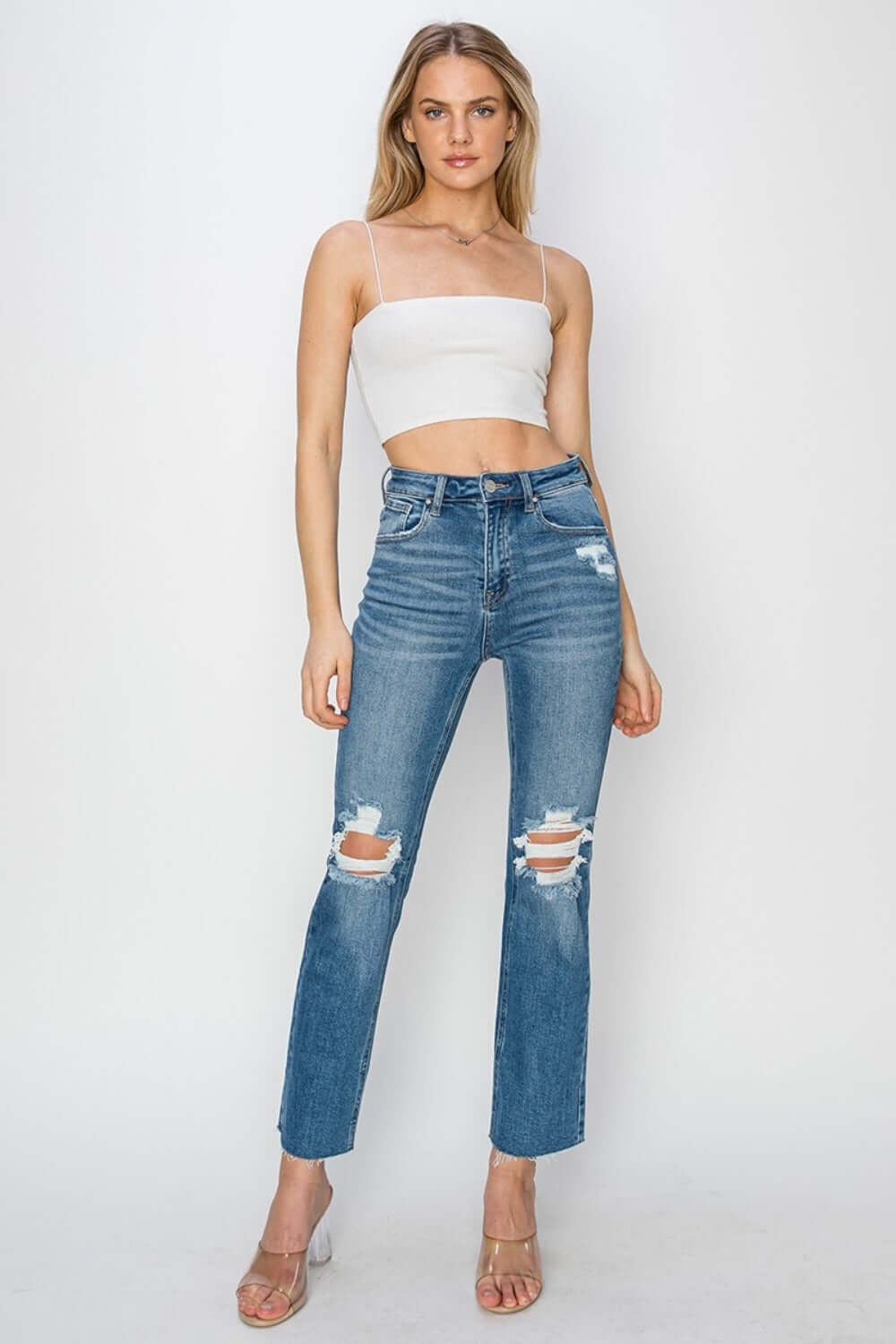 High rise distressed ankle Risen Jeans with trendy detailing and flattering fit, modeled with white crop top and clear heels.